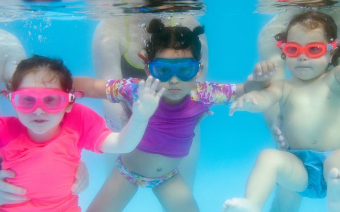 Toddlers moving underwater together in goggles
