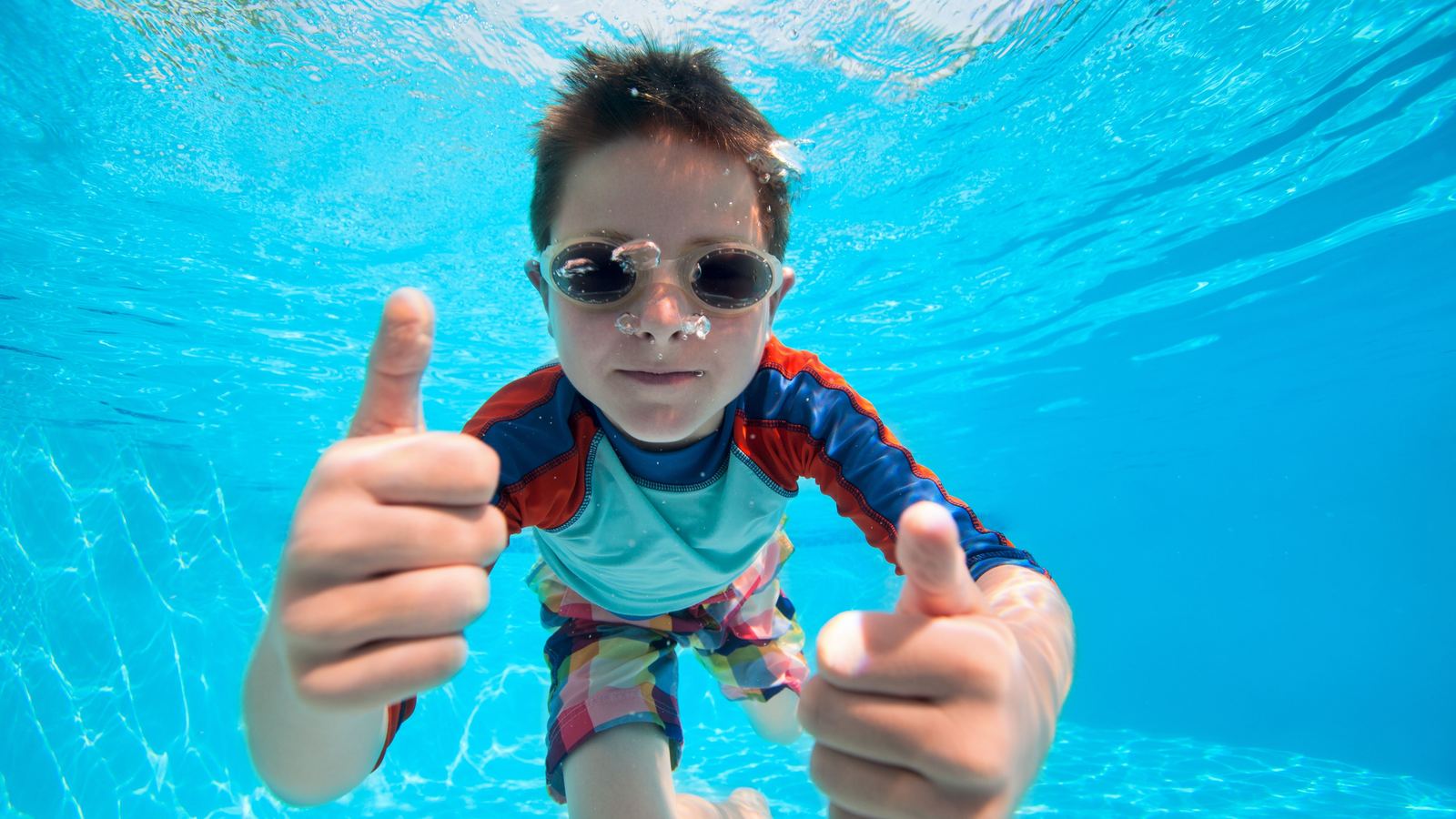 A child underwater giving two thumbs up