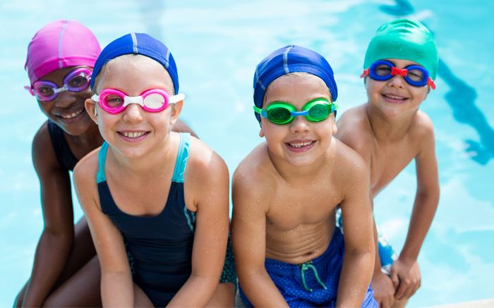 Four children in caps and goggles at the pool edge