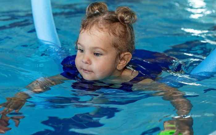 A toddler swimming between noodles during a Swimmable toddler class