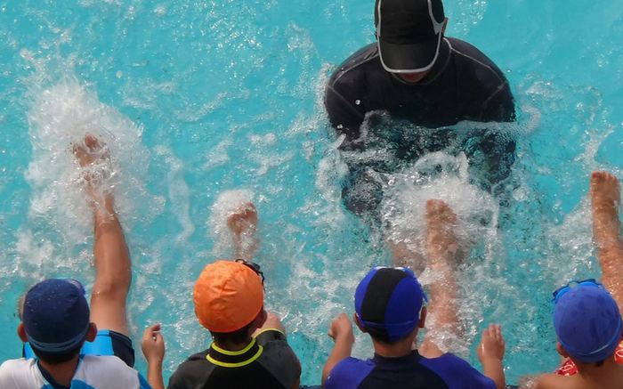 A group lesson practising kicking at the pool edge