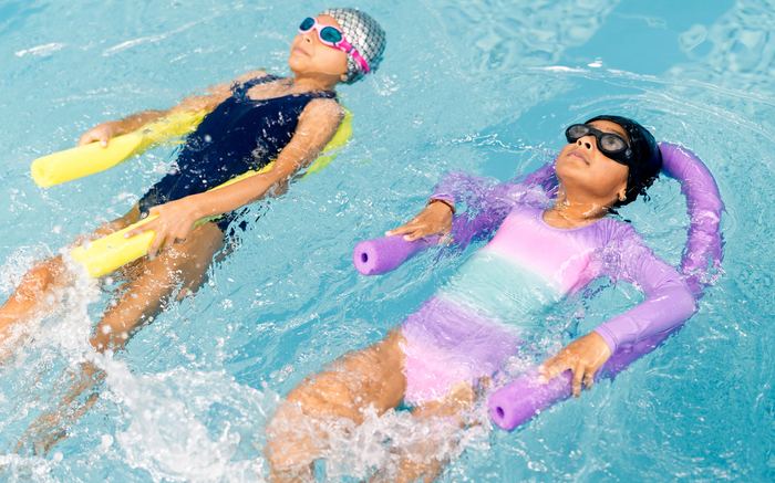Two young swimmers floating on pool noodles