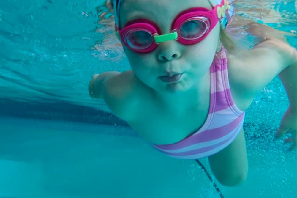 A toddler swimming towards the camera in goggles